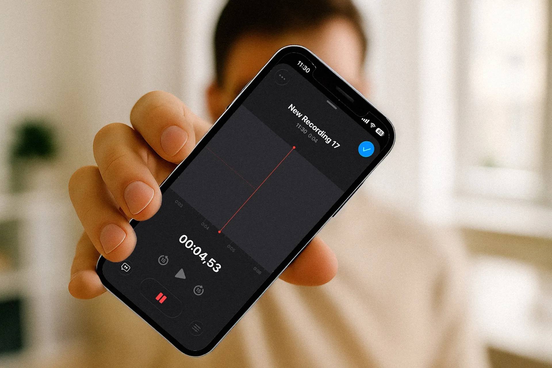Person holding a smartphone close to the camera showing a voice recording app screen with an active recording labeled New Recording 17 at 4.53 seconds.
